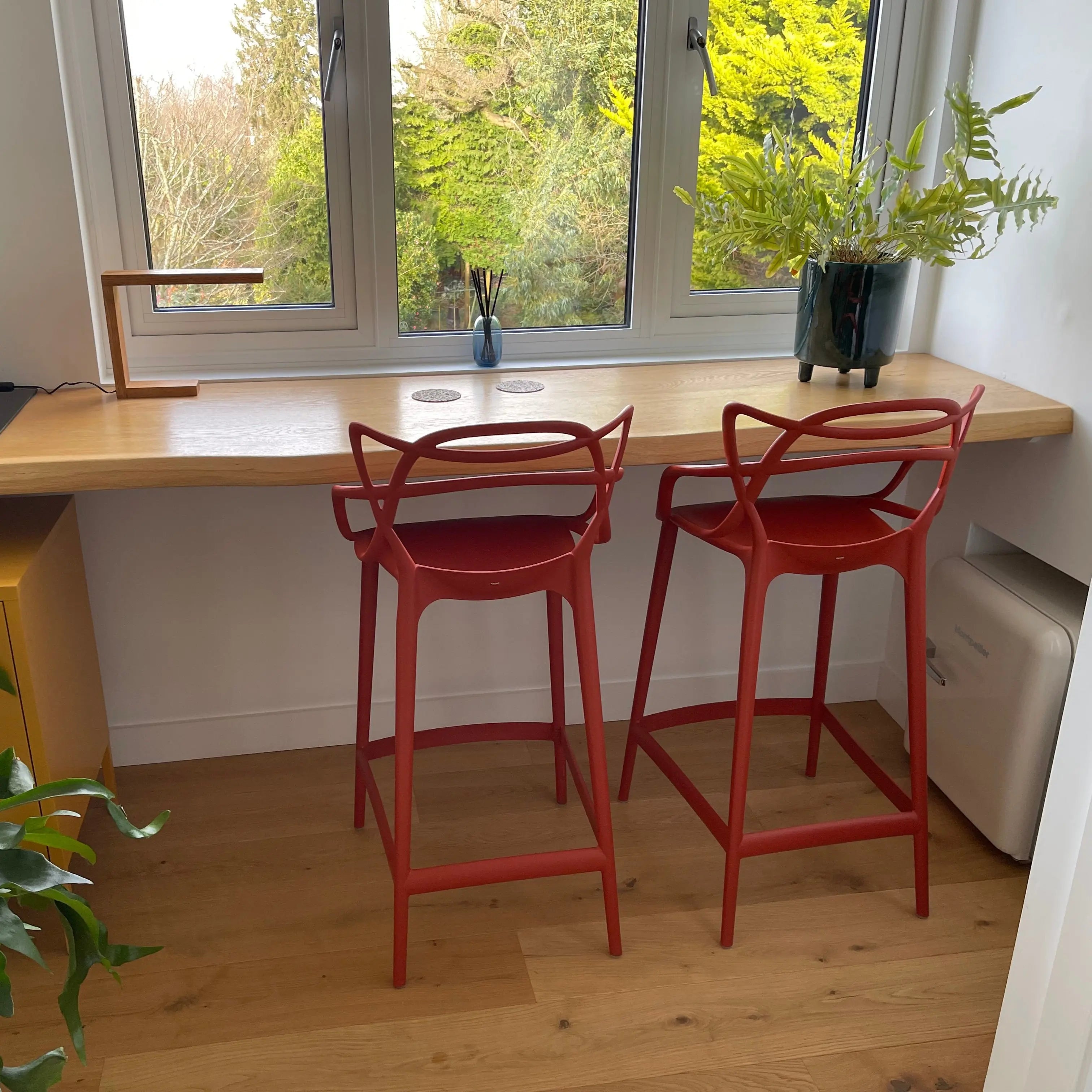 Wooden desk with red bar stools by a window with greenery outside