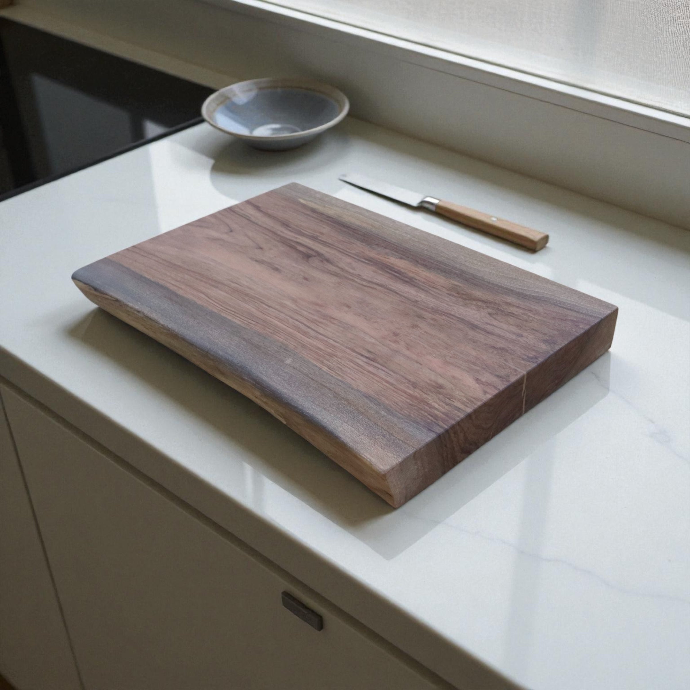 Wooden walnut cutting board with a knife on a white countertop
