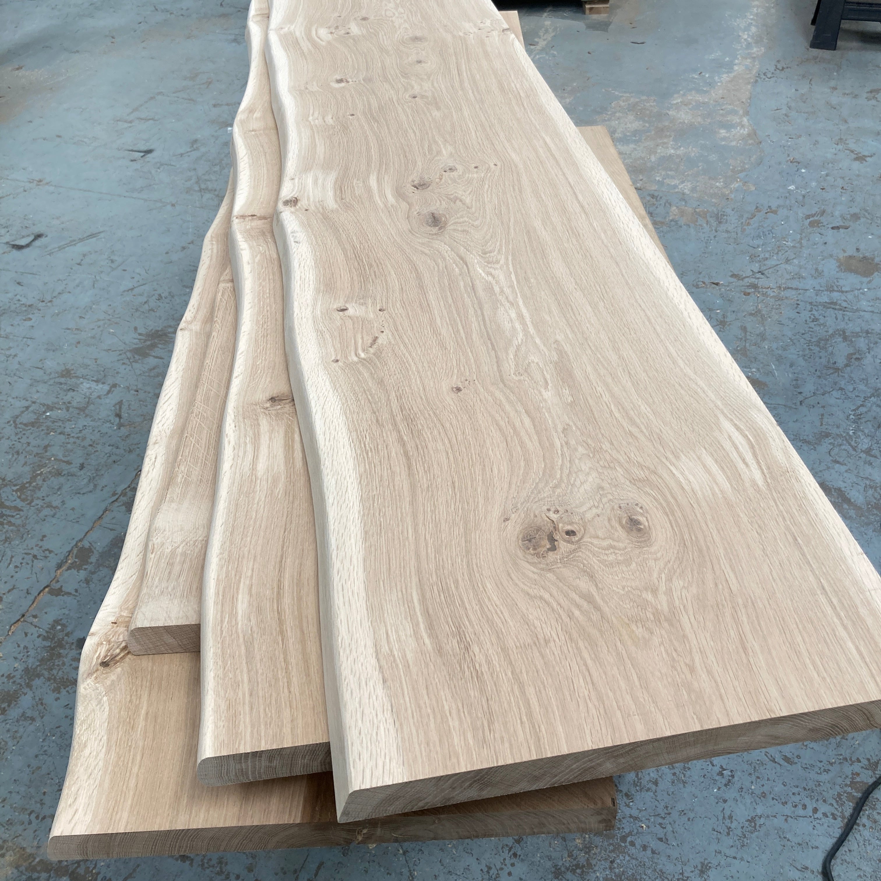 Stack of oak boards on a concrete floor with industrial equipment in the background