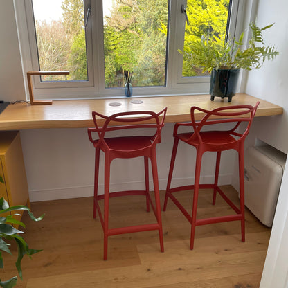 Wooden desk with red bar stools by a window with greenery outside